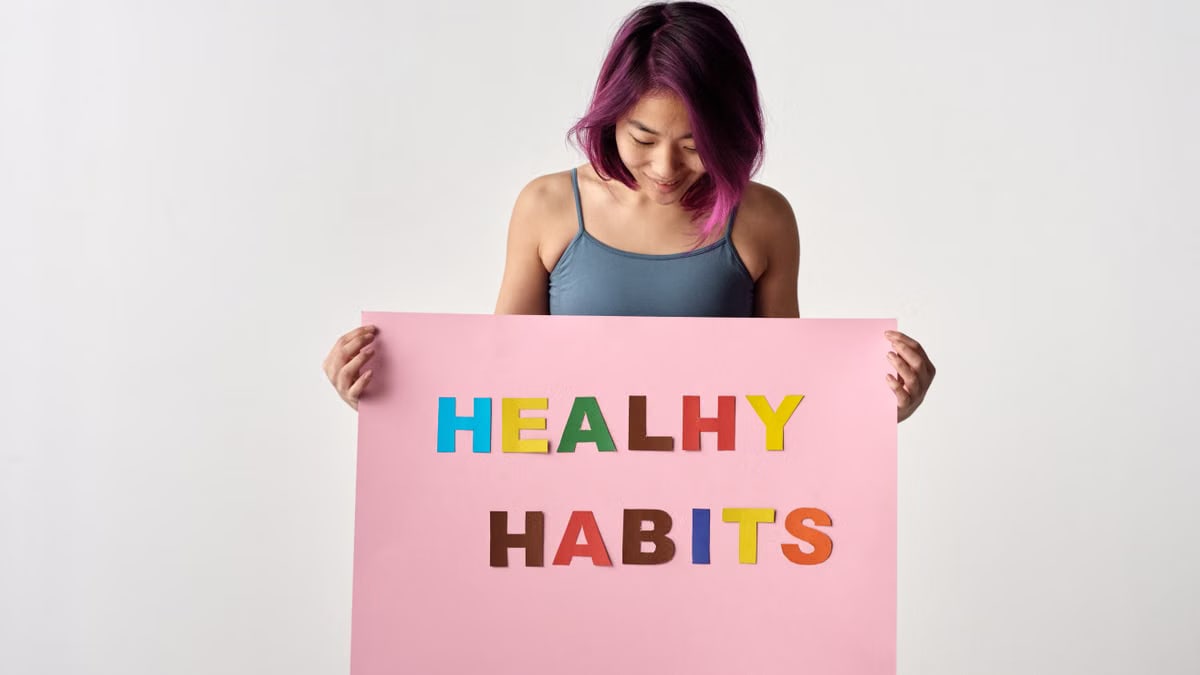 Asian woman holding a colorful 'Healthy Habits' sign in a studio setting, promoting wellness.
